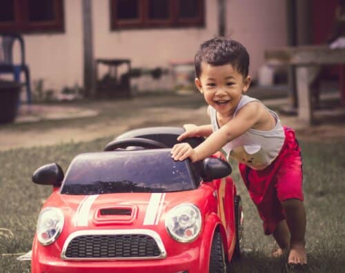 Little boy driving red car with the steering wheel. Little boy driving big toy car and having fun on grass outdoors.